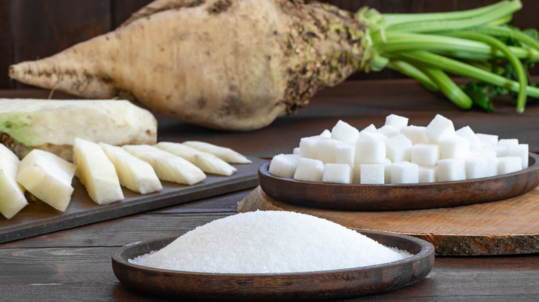 Granulated and cube sugar in bowl with fresh raw sugar beetroot on wooden table, beta vulgaris